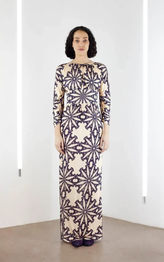 Model wearing a full-length silk jersey dress in beige and grey with long sleeves and an Eiffel Tower motif.